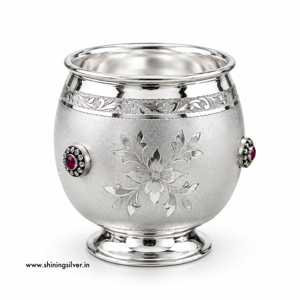 A sterling silver footed cup with an engraved floral motif on the front, a decorative band near the rim, and two red gemstone accents on the sides, shown on a white background.