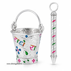 A silver-toned metal gift set featuring a small decorative bucket with a handle and a matching cylindrical pen or pointer, both decorated with colorful floral and script engravings. The bucket has the words 'Rati' in multicolored Devanagari script.