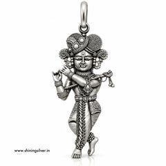 An intricate sterling silver pendant of a dancing Hindu deity, likely Lord Krishna, featuring detailed engravings, textured patterns, and a decorative headdress, shown on a plain white background with a website watermark.