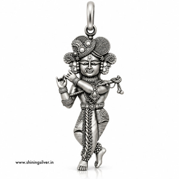 An intricate sterling silver pendant of a dancing Hindu deity, likely Lord Krishna, featuring detailed engravings, textured patterns, and a decorative headdress, shown on a plain white background with a website watermark.