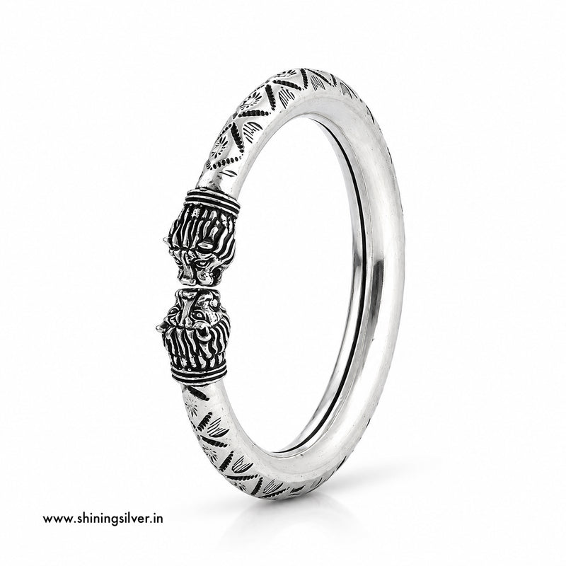 A sterling silver band ring with detailed lion head carvings and geometric patterns on the band, shown on a clean white background.