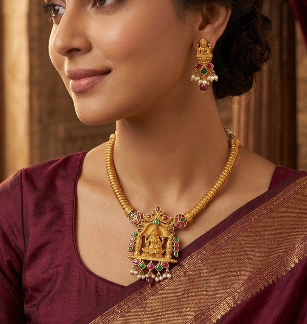 Woman wearing gold jewelry with a maroon saree against a neutral background