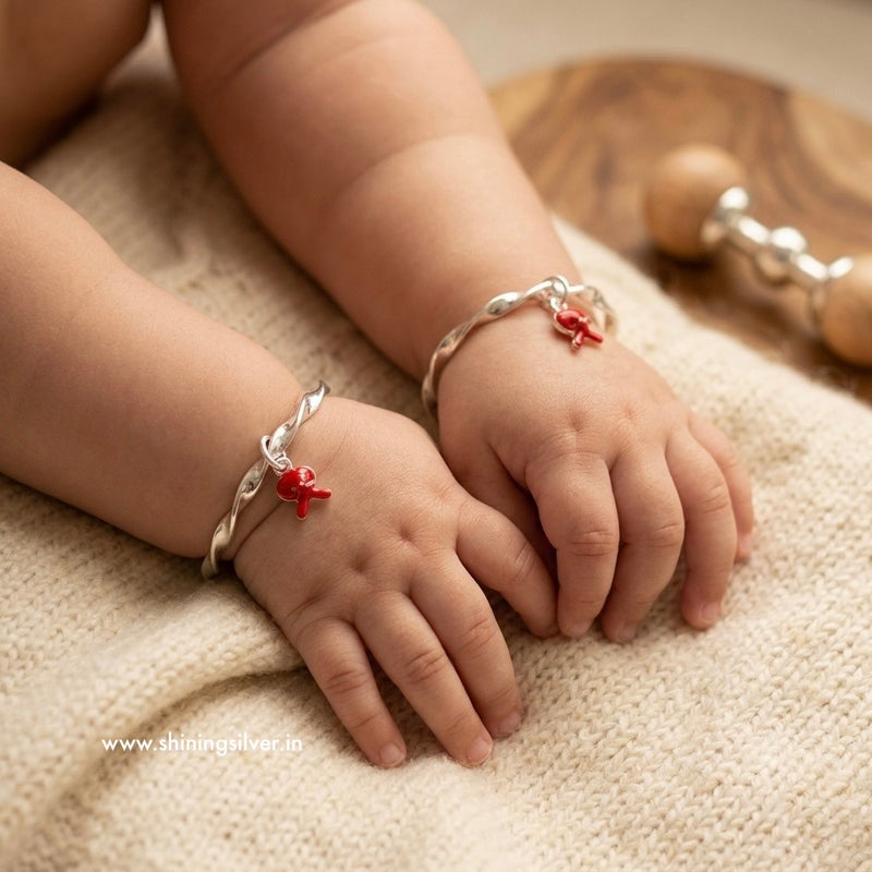 Child's hands wearing silver bracelets with red charms on a soft surface. Shiningsilver.in