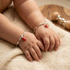 Child's hands wearing silver bracelets with red charms on a soft surface. Shiningsilver.in