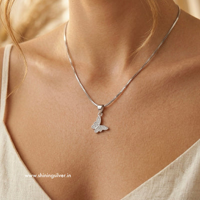 Silver butterfly necklace on a person's neck with a neutral background, shining silver