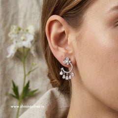 Close-up of a woman wearing silver earrings with a blurred background and floral element. “ shiningsilver.in “