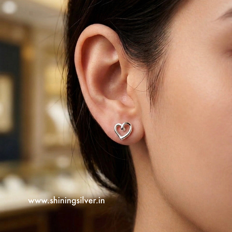 Heart-shaped earring worn by a person with a blurred background. shininsilver.in