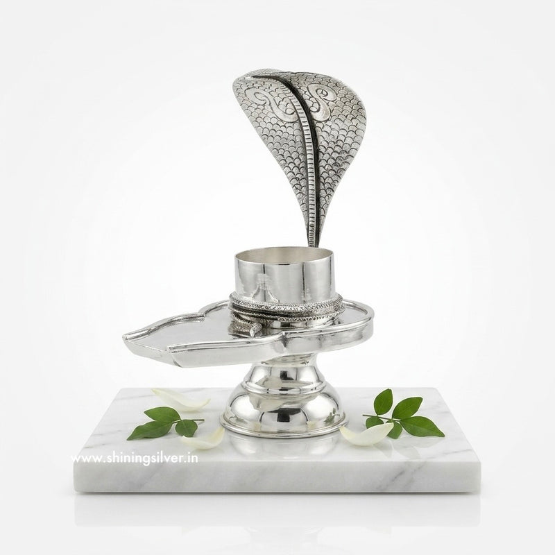 Silver Shiva jalheri shivling stand on a marble base with floral designs, brand 'Shining Silver' visible.