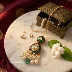 Ornate mang tika with green and red accents on a marble surface with a flower and jewelry box.