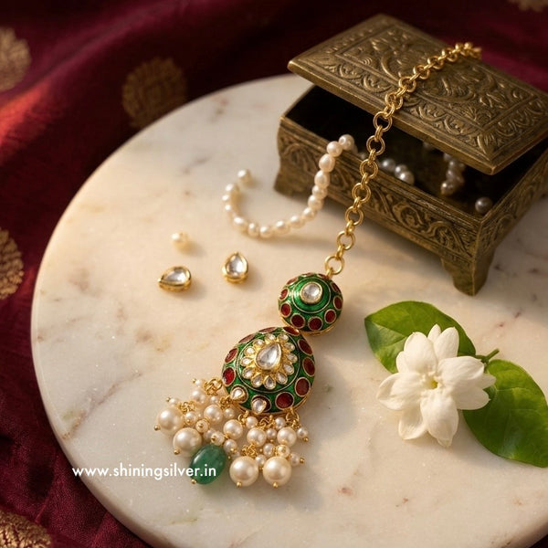 Ornate mang tika with green and red accents on a marble surface with a flower and jewelry box.
