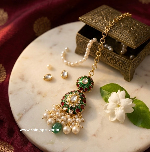 Ornate mang tika with green and red accents on a marble surface with a flower and jewelry box.