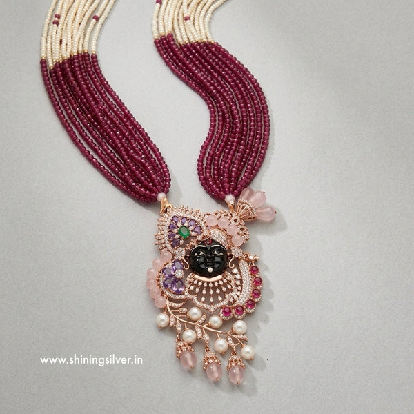 Ornate necklace with maroon beads and a detailed shrinath ji pendant on a gray background
