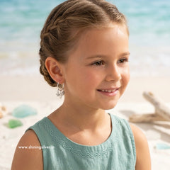 Young girl with braided hair on a beach, wearing silver earrings.