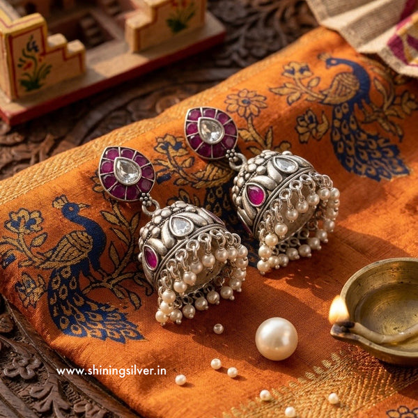 Silver earrings with pearls and red stones on a decorative fabric background