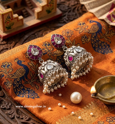 Silver earrings with pearls and red stones on a decorative fabric background